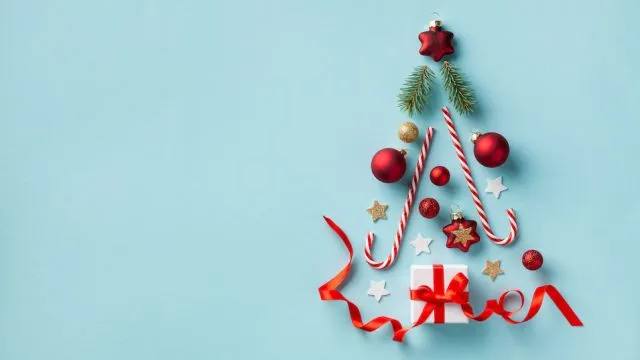 Creative Christmas fir tree made of gift box and holiday decorations on blue background top view. New Year greeting card. Flat lay.