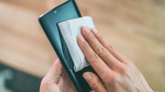 Cleaning mobile phone screen with disinfecting wet wipes for clean smartphone preventive wiping for COVID-19 Coronavirus outbreak contamination prevention.