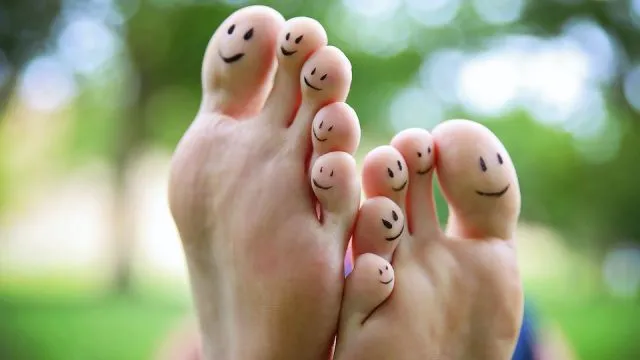 smiley faces on a pair of feet on all ten toes in a park on a hot summer day